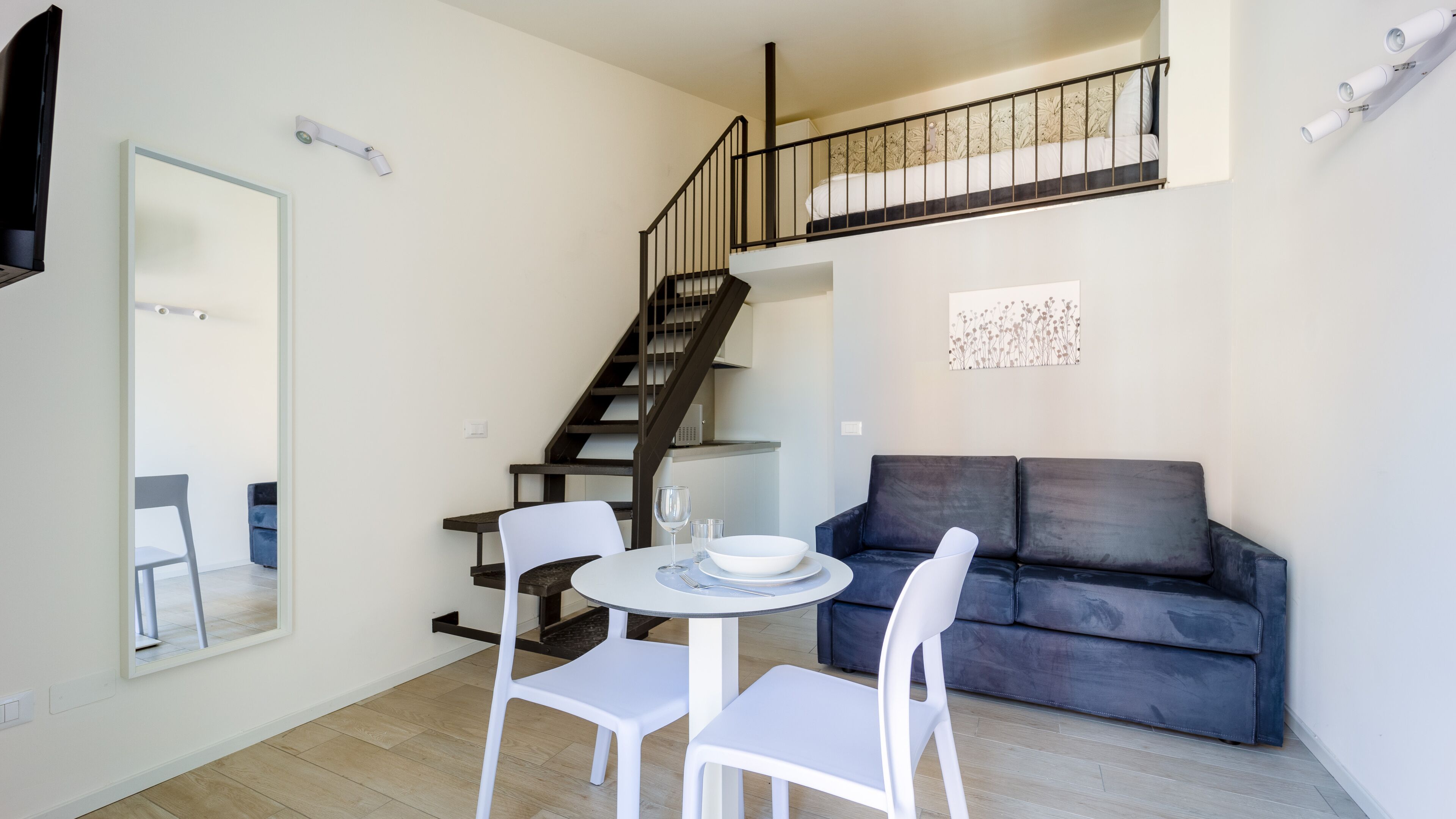 A modern living room with a staircase, a dining area with a table and chairs, and a dark-colored sofa.