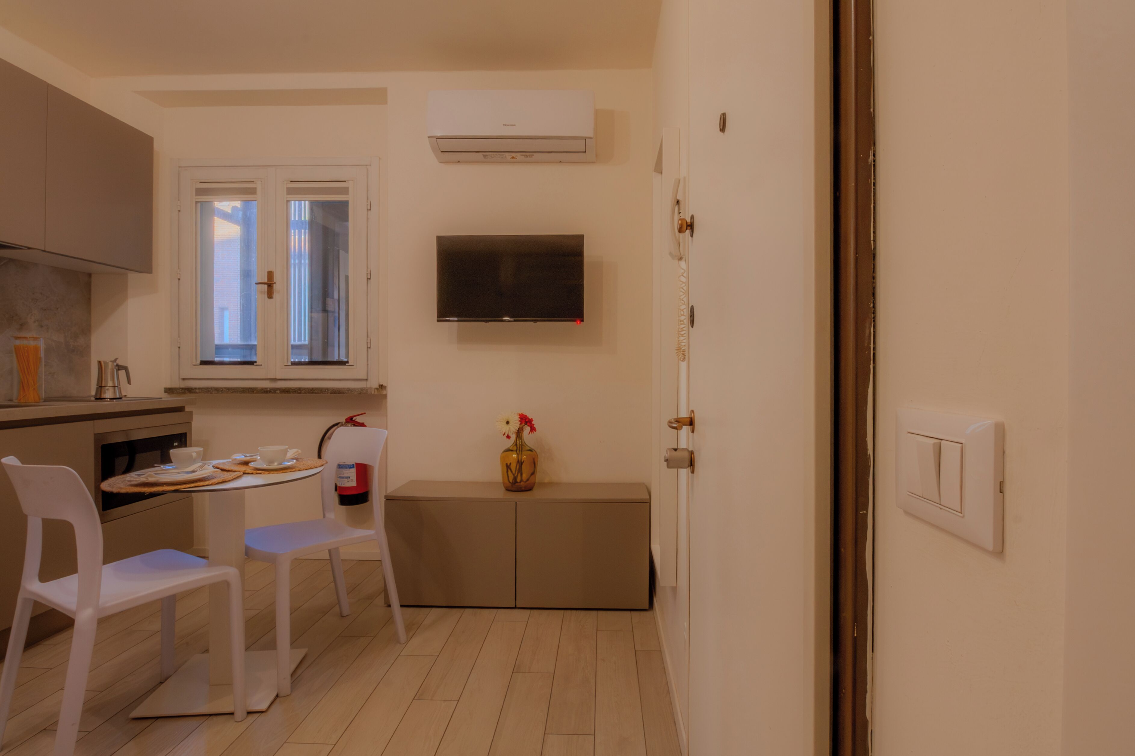 Une cuisine compacte avec un coin repas, un téléviseur fixé au mur et une porte donnant sur une autre pièce.