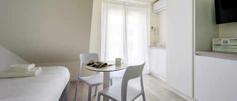 Ein Hotelzimmer mit einem Bett, einem kleinen Tisch mit Stuhl, einer Kaffeetasse, einem Telefon und einer Klimaanlage.