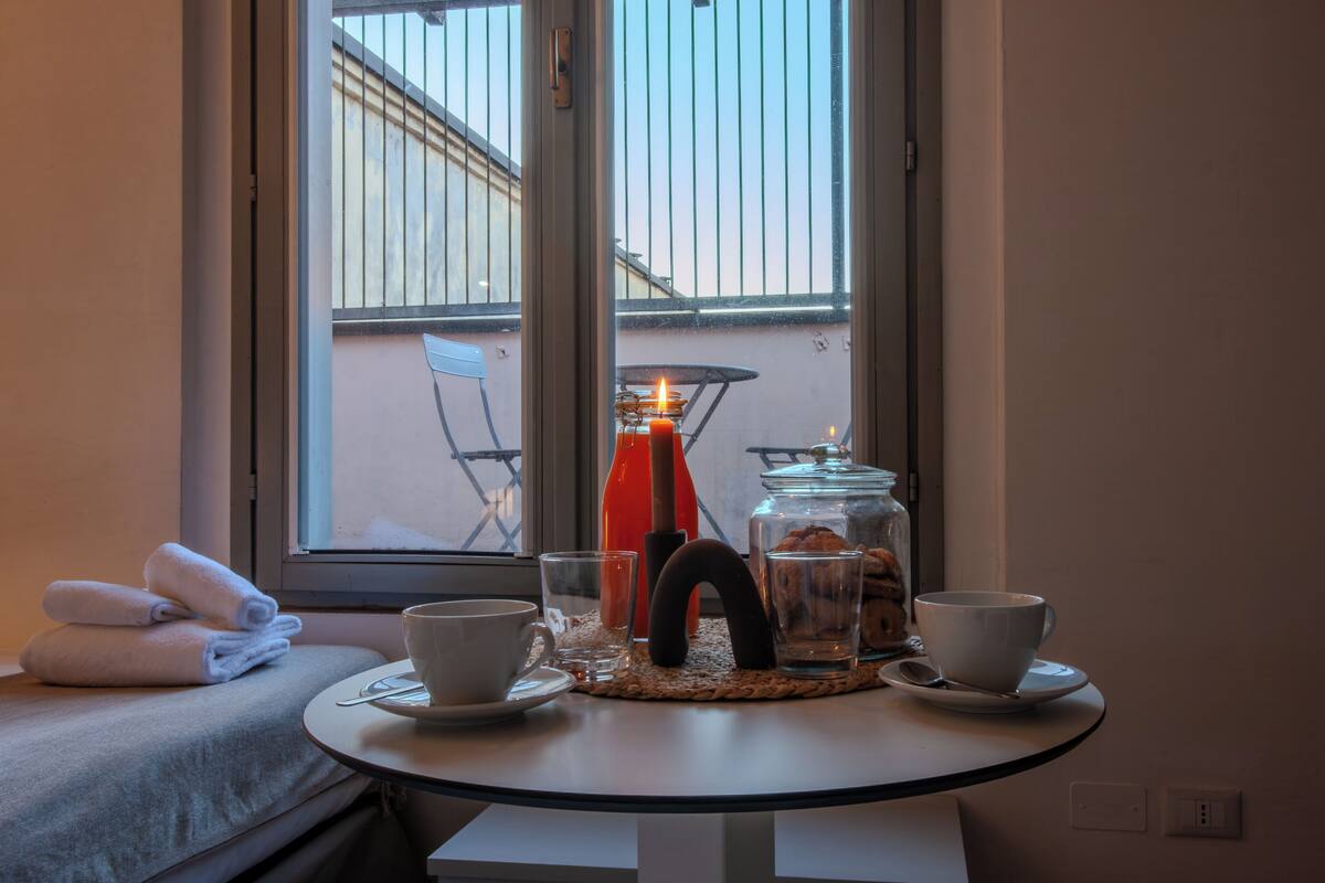 A small round table with two white cups, a glass, and a jar of cookies. There are towels on a bench to the left.