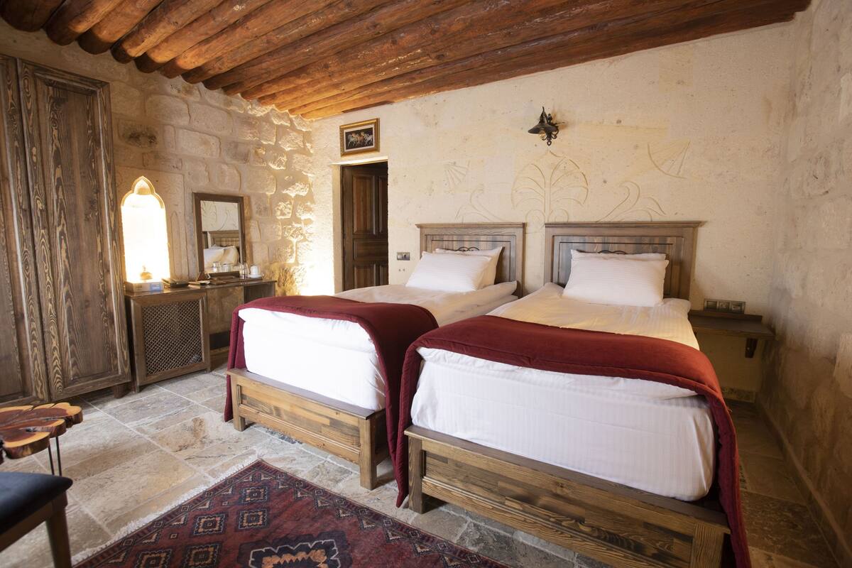 A rustic bedroom with two wooden beds, a stone wall, and a wooden ceiling.