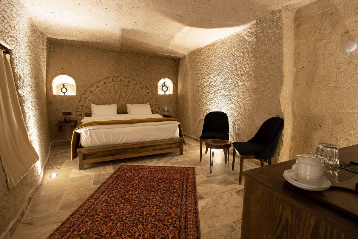 A cozy bedroom with a large bed, a chair, a small table with a cup and saucer, and a rug.