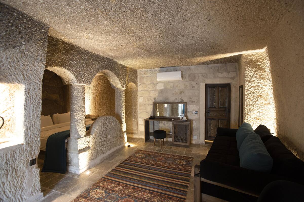 A stone-walled room with a bed, a sofa, and a small table with a mirror.
