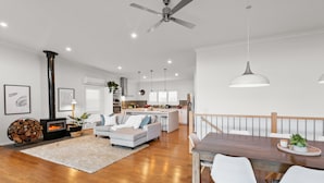 A modern living room with a fireplace, a dining area with a wooden table and white chairs, and a kitchen in the background. - Bridge Water Views - Waterfront (Bonnie Doon)