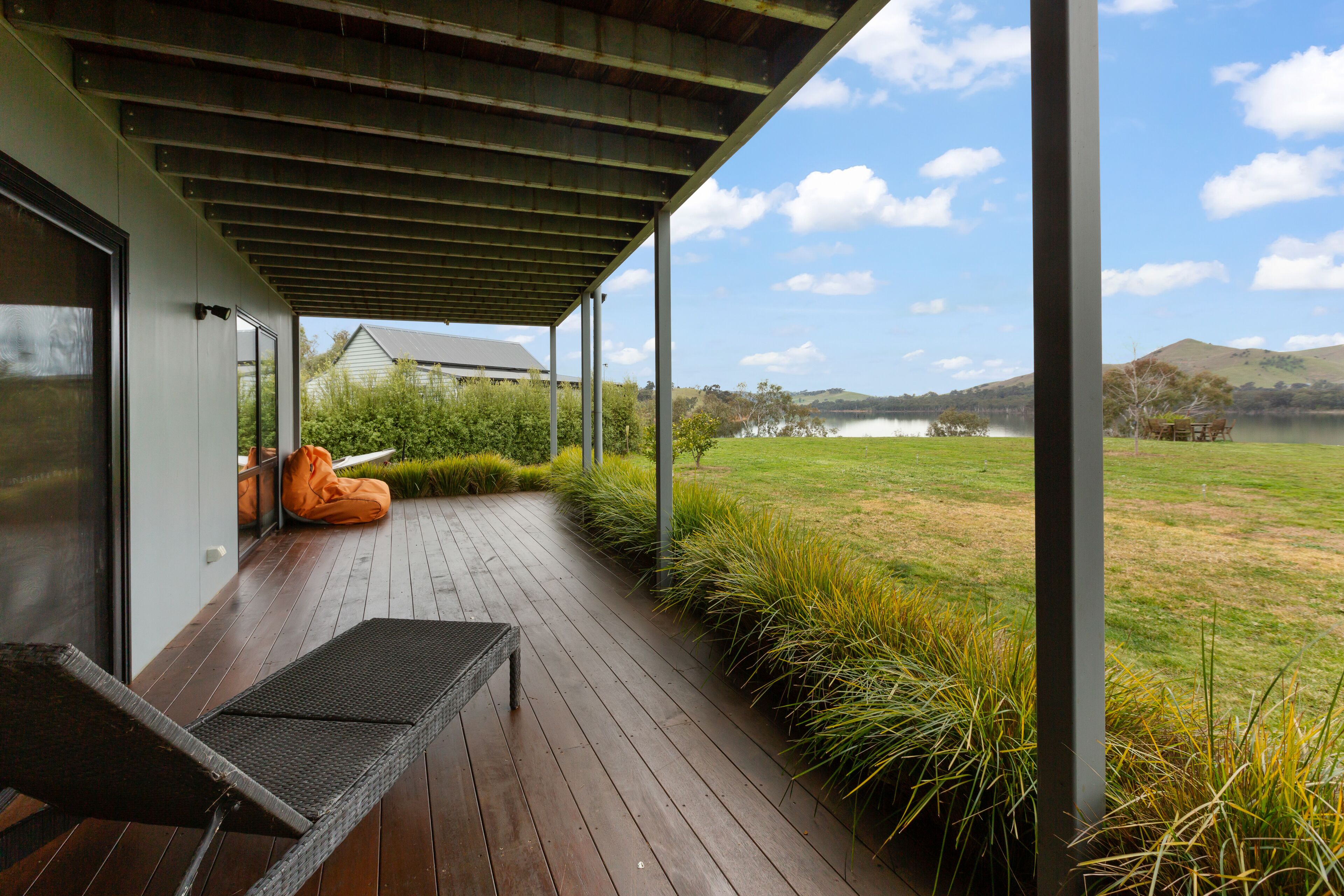 A covered outdoor area with a bench, a view of a lake, and a grassy landscape.