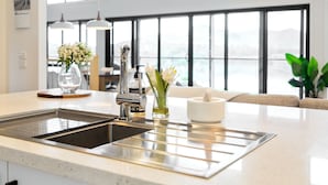 A modern kitchen with a stainless steel sink, a vase with flowers, and a view of the outdoors through large windows. - Bridge Water Views - Waterfront (Bonnie Doon)
