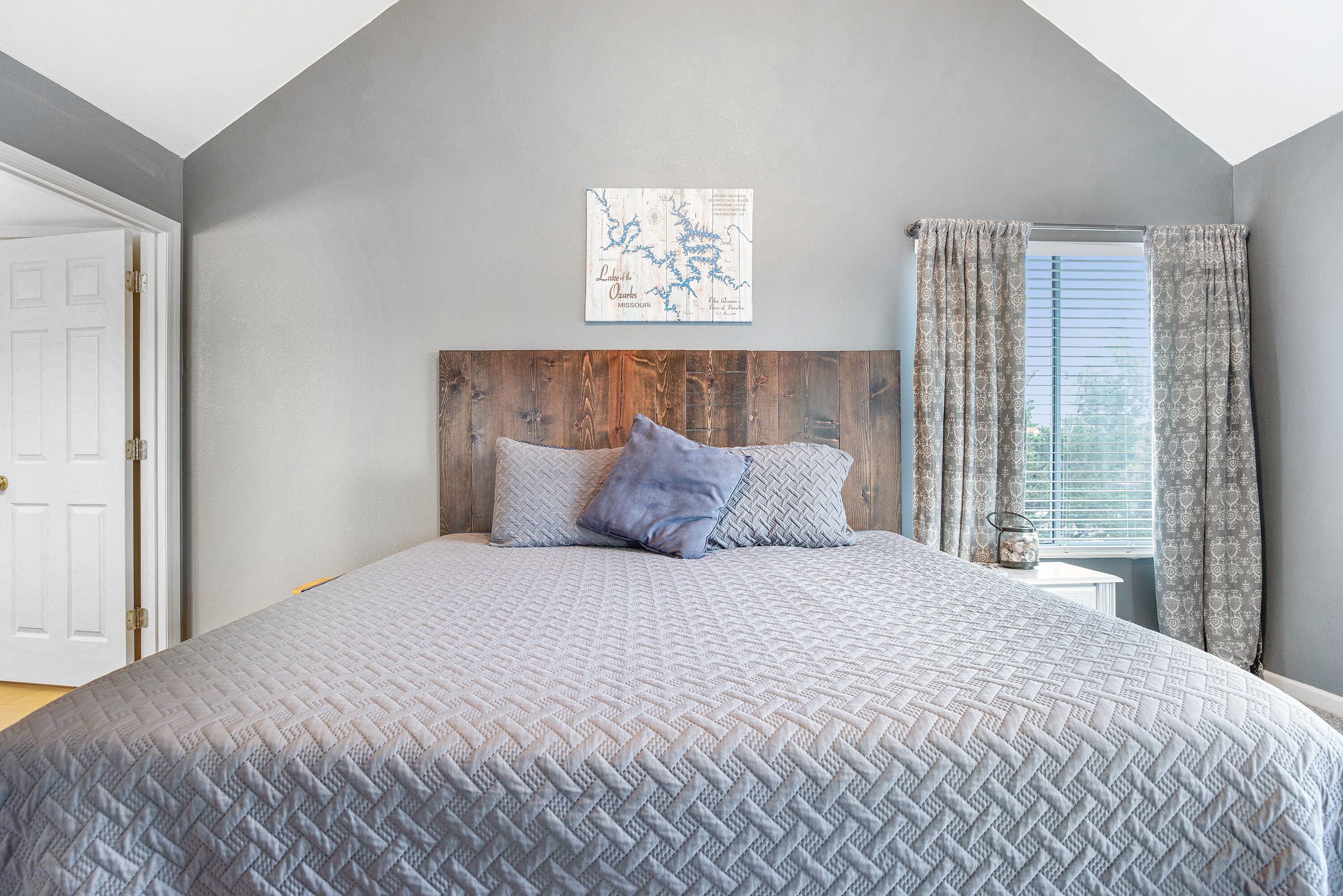 A bedroom with a large bed, a wooden headboard, a map on the wall, and a window with curtains.