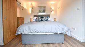 A bedroom with a large bed, wooden wardrobe, and wall-mounted lights. - Cheerful 1BD Cottage With Parking Nr Guildford (Guildford)