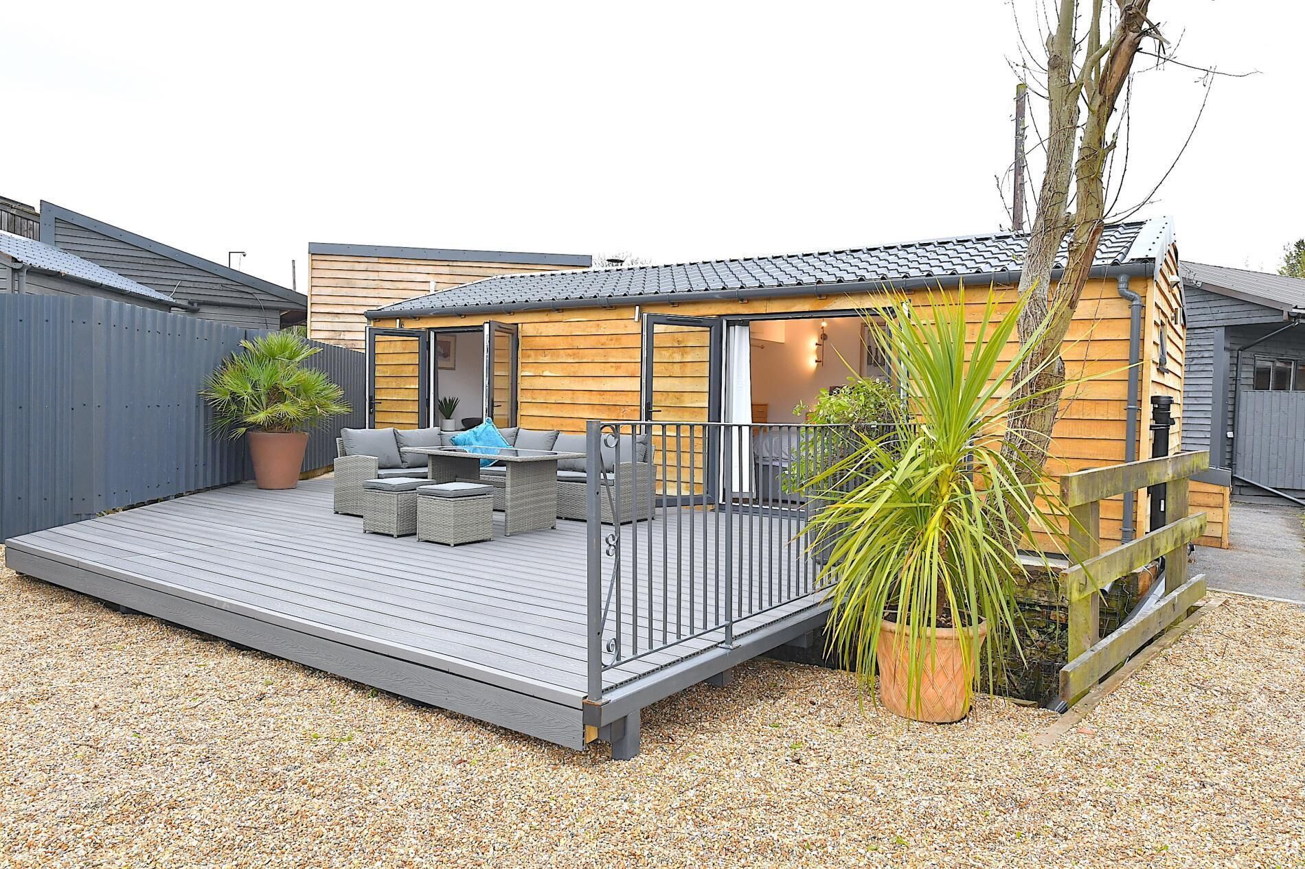 A modern outdoor deck with a sofa and chairs, surrounded by a wooden fence and potted plants.