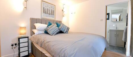 A bedroom with a bed, bedside table, lamp, and a framed picture on the wall.