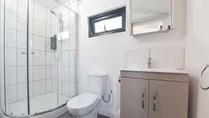 A bathroom with a glass shower enclosure, a toilet, a sink with a mirror, and a cabinet. - Cheerful 1BD Cottage With Parking Nr Guildford (Guildford)