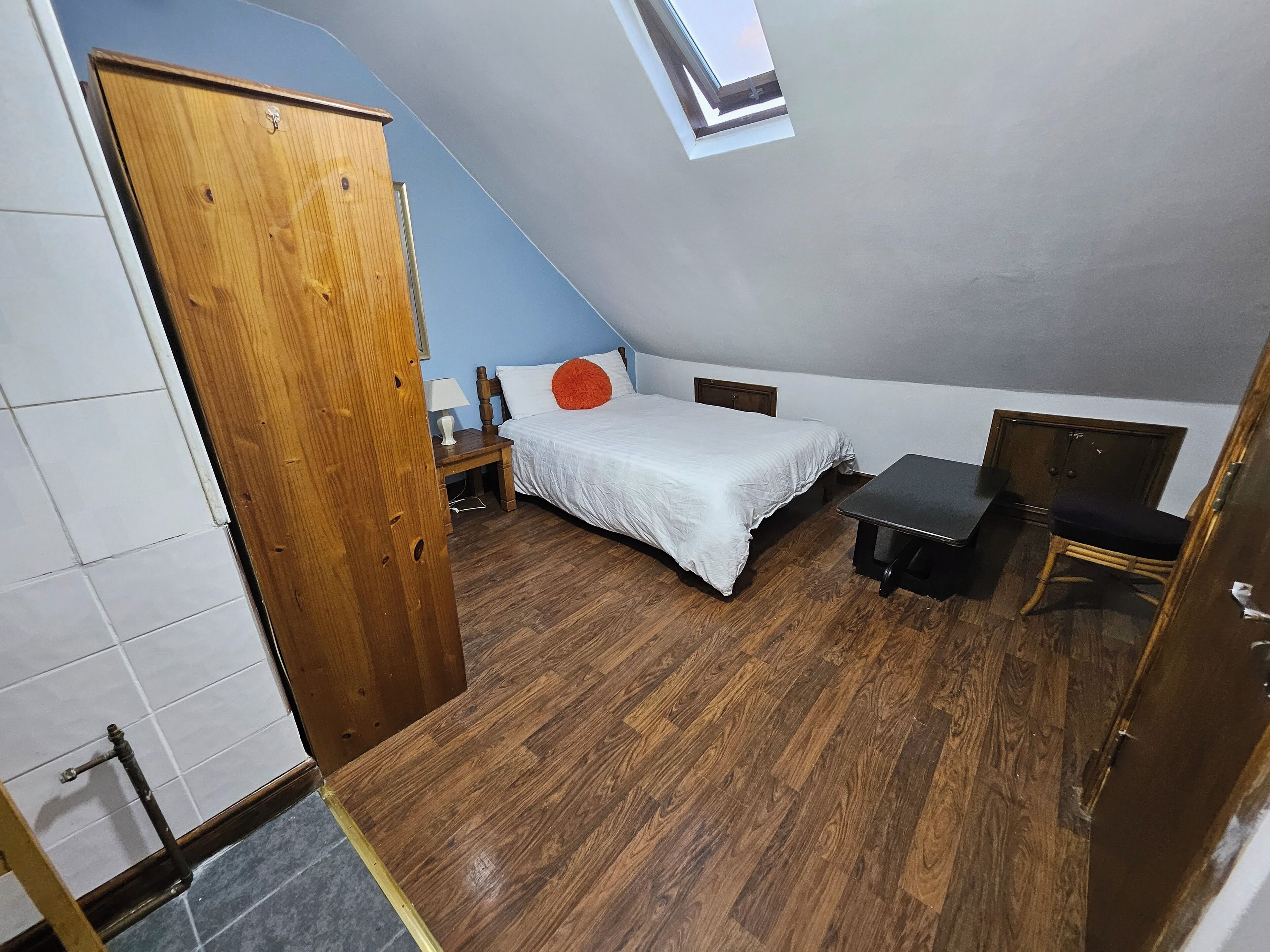 A small, compact room with a bed, a desk, a chair, and a wardrobe.