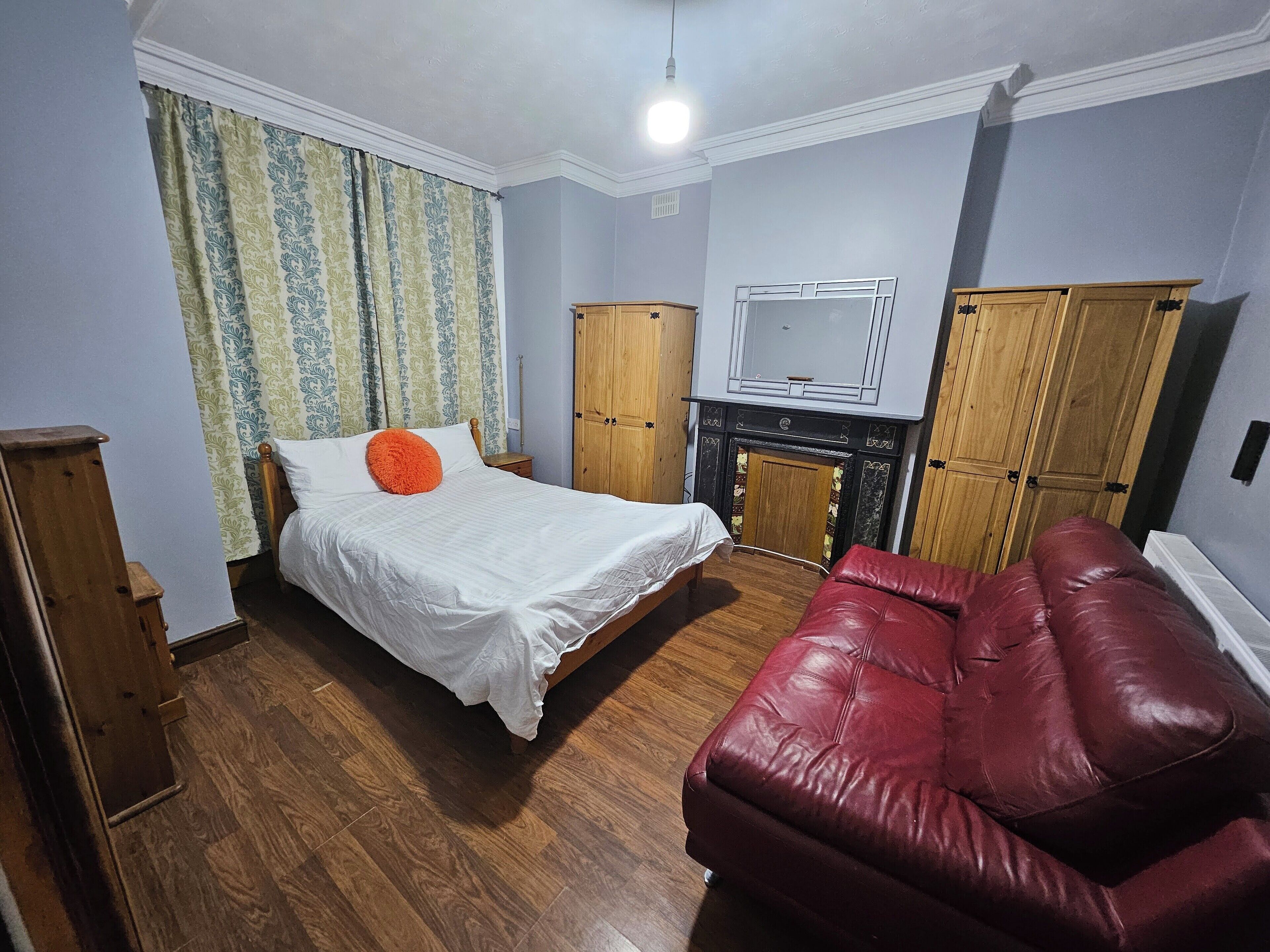Quarto com cama, sofá de couro vermelho, guarda-roupa de madeira e televisão.