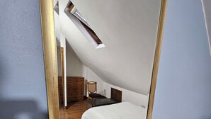 Un dormitorio con un espejo grande, una cama, un aparador de madera y una mesita de noche.