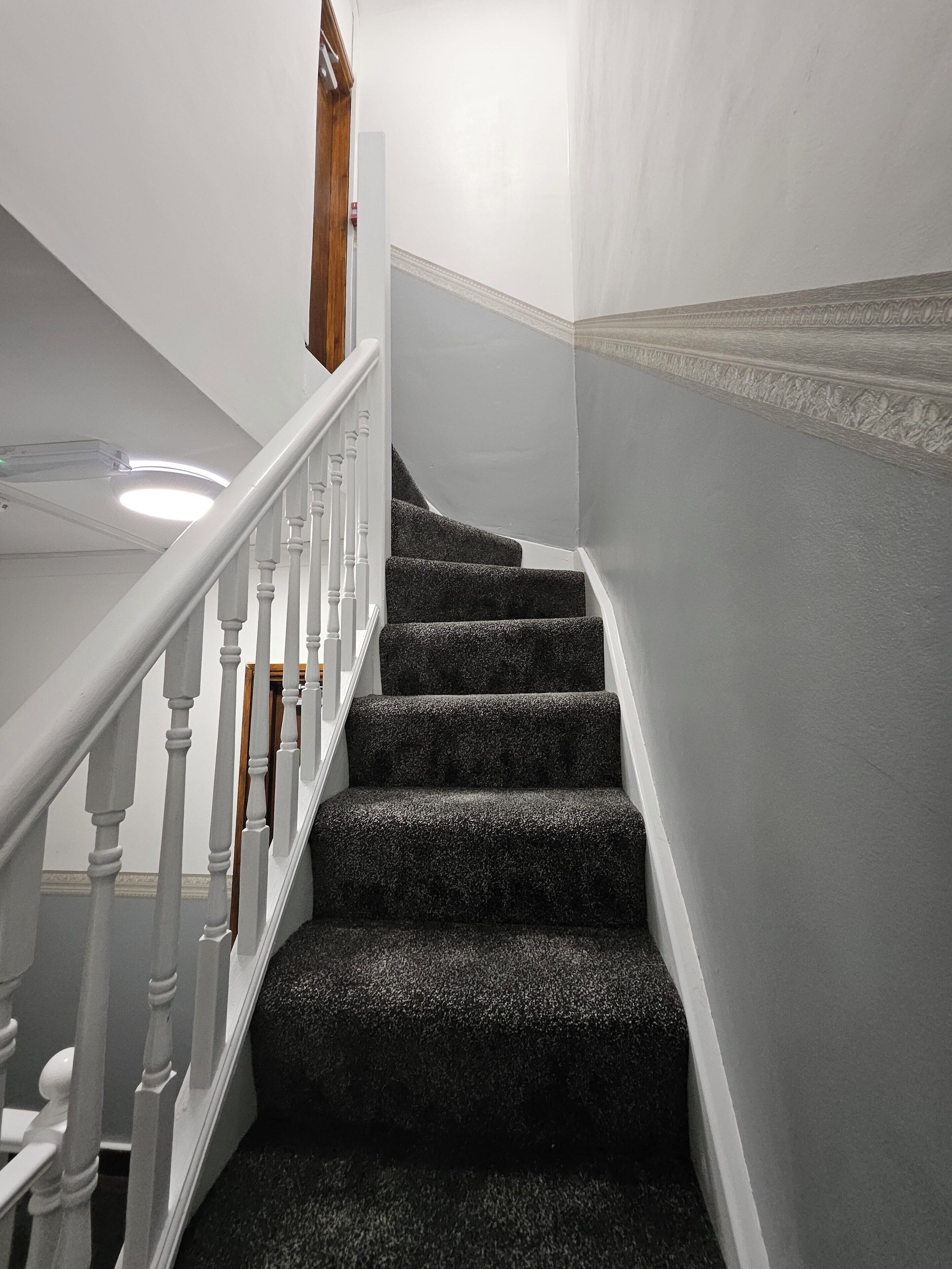 Una escalera con balaustres blancos y peldaños alfombrados oscuros.