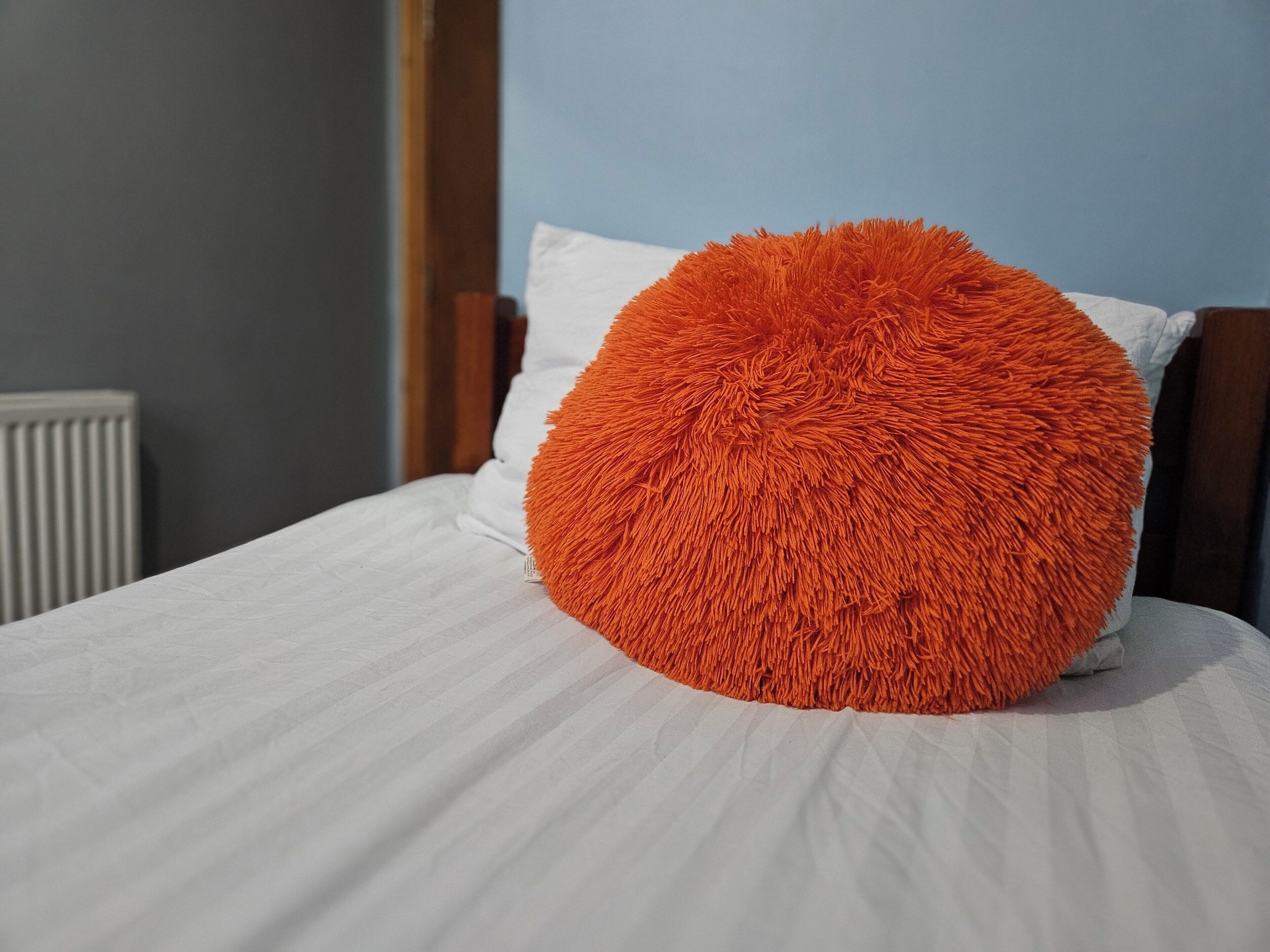 A bed with a white sheet and a single orange textured pillow.