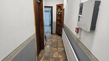 A hallway with a tiled floor, a radiator, a wooden door, and a wall-mounted electrical box.