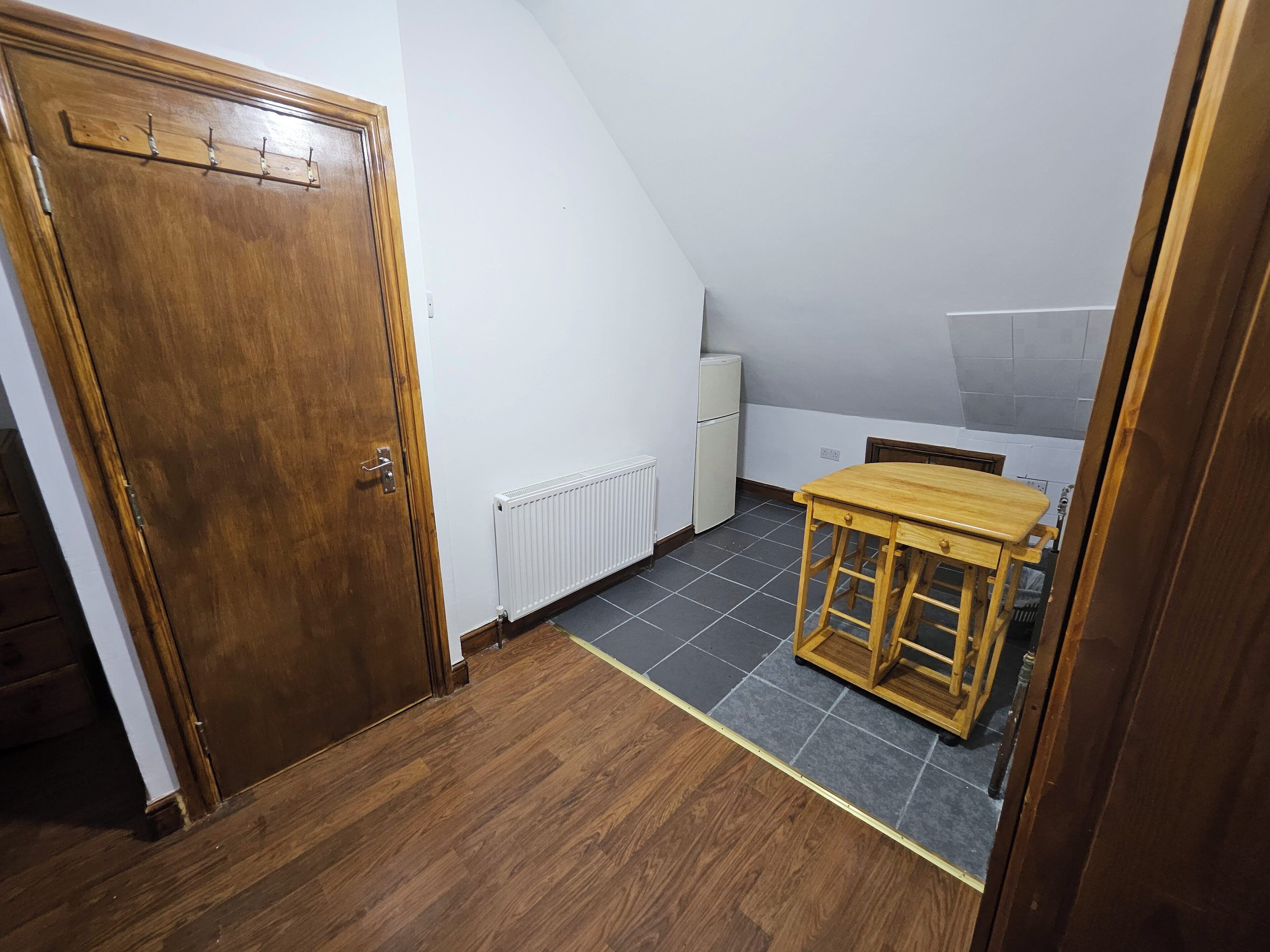 Et værelse med dør i træ, en radiator, en lille hvid apparat og et træbord.