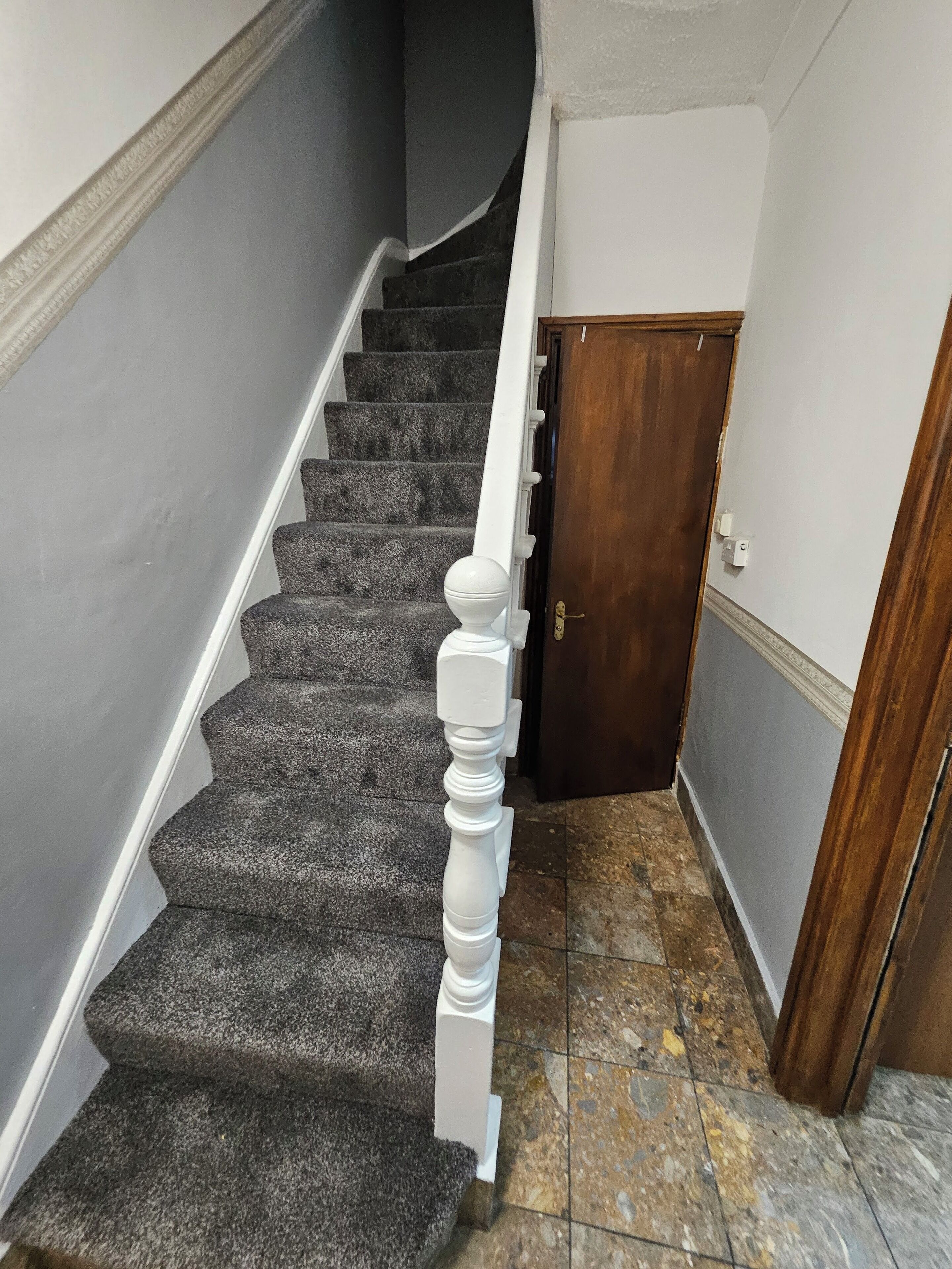 A staircase with carpeted steps, white balusters, and a wooden door at the top.