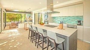 A modern kitchen with a central island, bar stools, and a view of the outdoors. - Casa La Reina, Private Jungle Villa (Tamarindo)