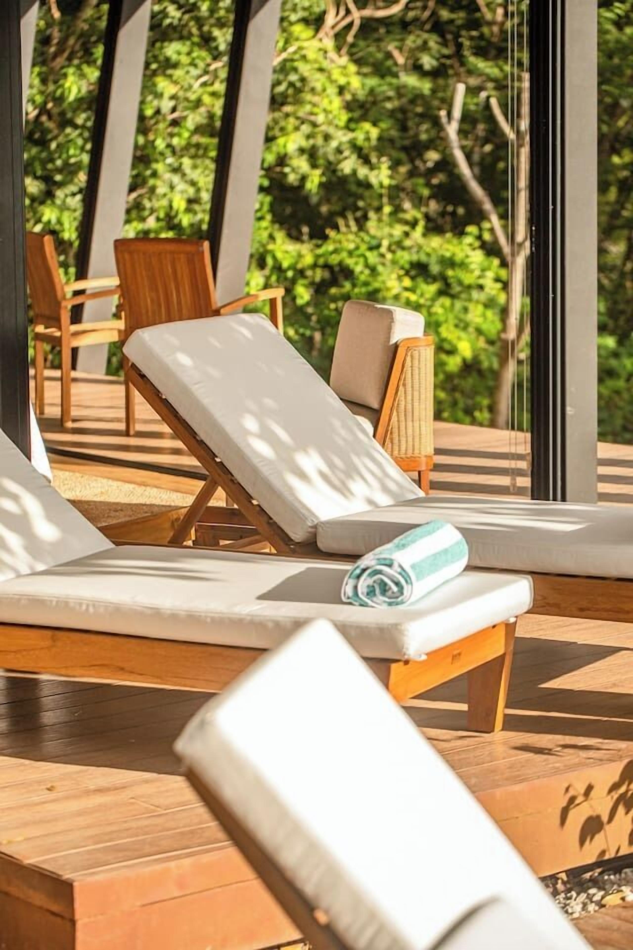 A sunlit outdoor lounge area with wooden loungers and a view of lush greenery.
