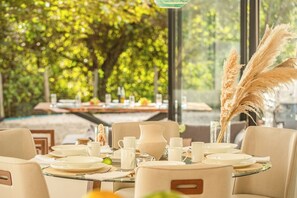 Un comedor con mesas redondas, sillas y vistas al verde exterior.