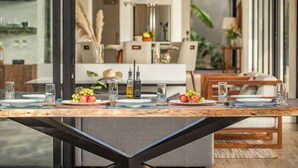 A dining table set with plates, glasses, and fruit, with a modern interior and large windows. - Casa La Reina, Private Jungle Villa (Tamarindo)