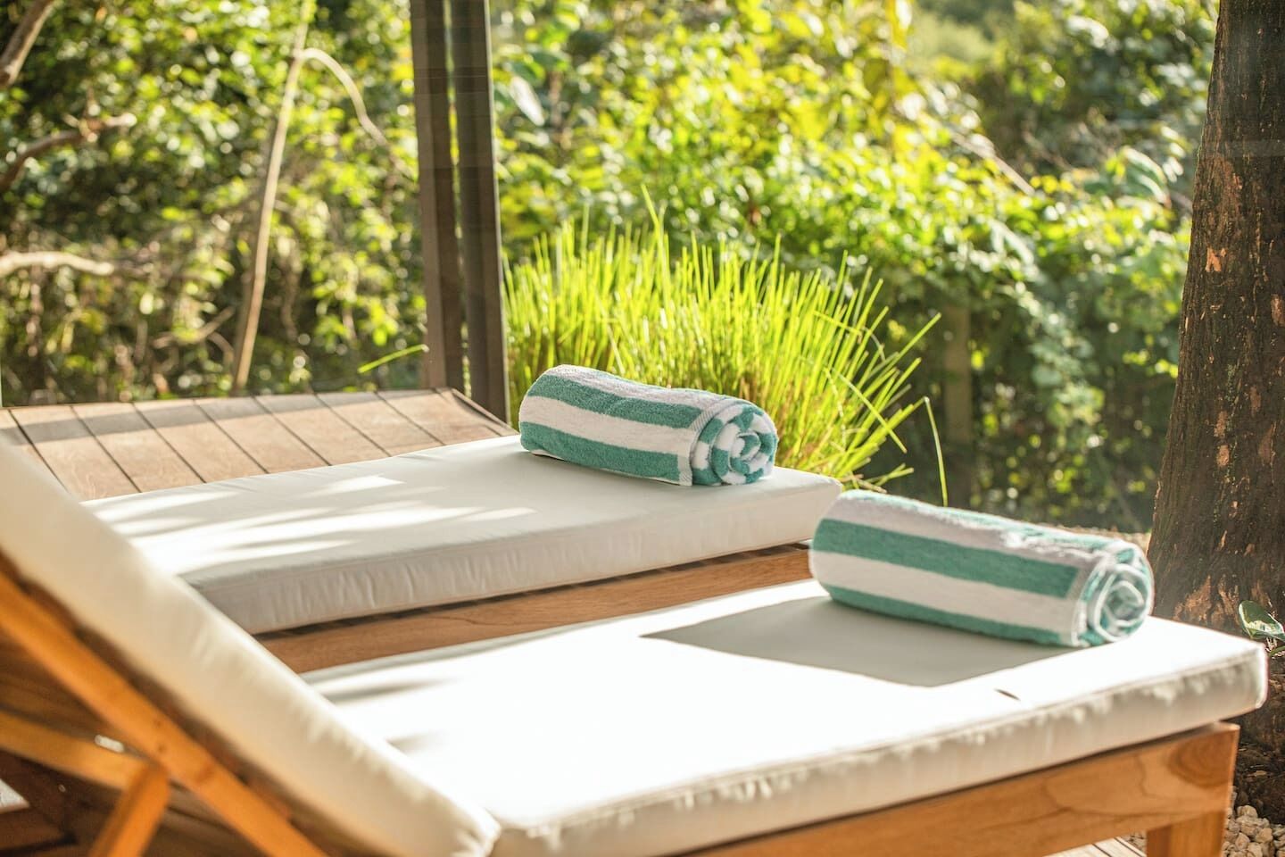 Una terraza de madera con dos sillas reclinables blancas, cada una con una toalla enrollada.