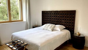A bedroom with a large bed, a wooden headboard, a bedside table, and a window with curtains.