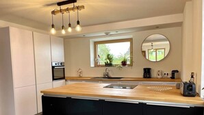 A modern kitchen with a wooden countertop, black cabinets, a built-in oven, and a window with a view of greenery.