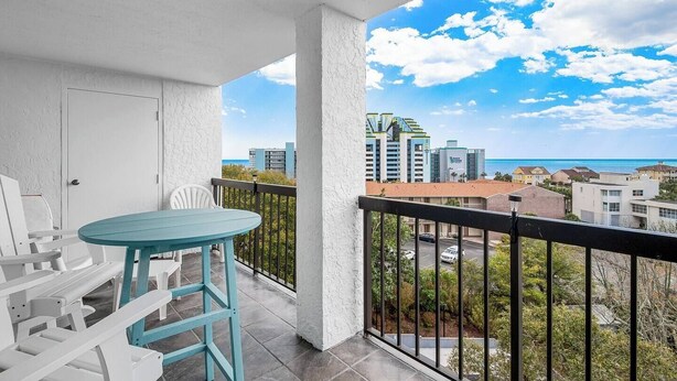 A balcony with a turquoise table and white chairs, overlooking a cityscape and the ocean. - Ocean View 3BR Suite: Beachside Escape (Myrtle Beach)