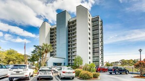 A modern multi-story building with a parking lot in front. - Ocean View 3BR Suite: Beachside Escape (Myrtle Beach)