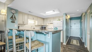 A kitchen with a central island, bar stools, and a microwave. - Ocean View 3BR Suite: Beachside Escape (Myrtle Beach)