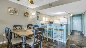 A dining area with a wooden table and chairs, a ceiling fan, and a kitchen with light blue cabinets and a microwave. - Ocean View 3BR Suite: Beachside Escape (Myrtle Beach)