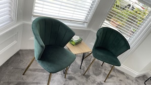 Twee groene bekleden stoelen met houten poten, een klein houten tafeltje en een doos op het tafeltje.