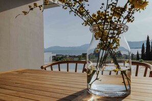 A clear glass vase with yellow flowers on a wooden table, overlooking a body of water and mountains. - Villa Pelagia Summary (Paleros)