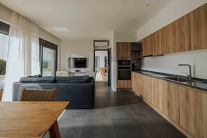 A modern kitchen with wooden cabinets, a black countertop, and a built-in oven. - Villa Pelagia Summary (Paleros)