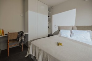 Un dormitorio con una cama grande, un armario, una silla y un estante con libros y objetos decorativos.