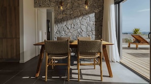 A dining area with a stone wall, wooden table, and wicker chairs. - Villa Pelagia Summary (Paleros)