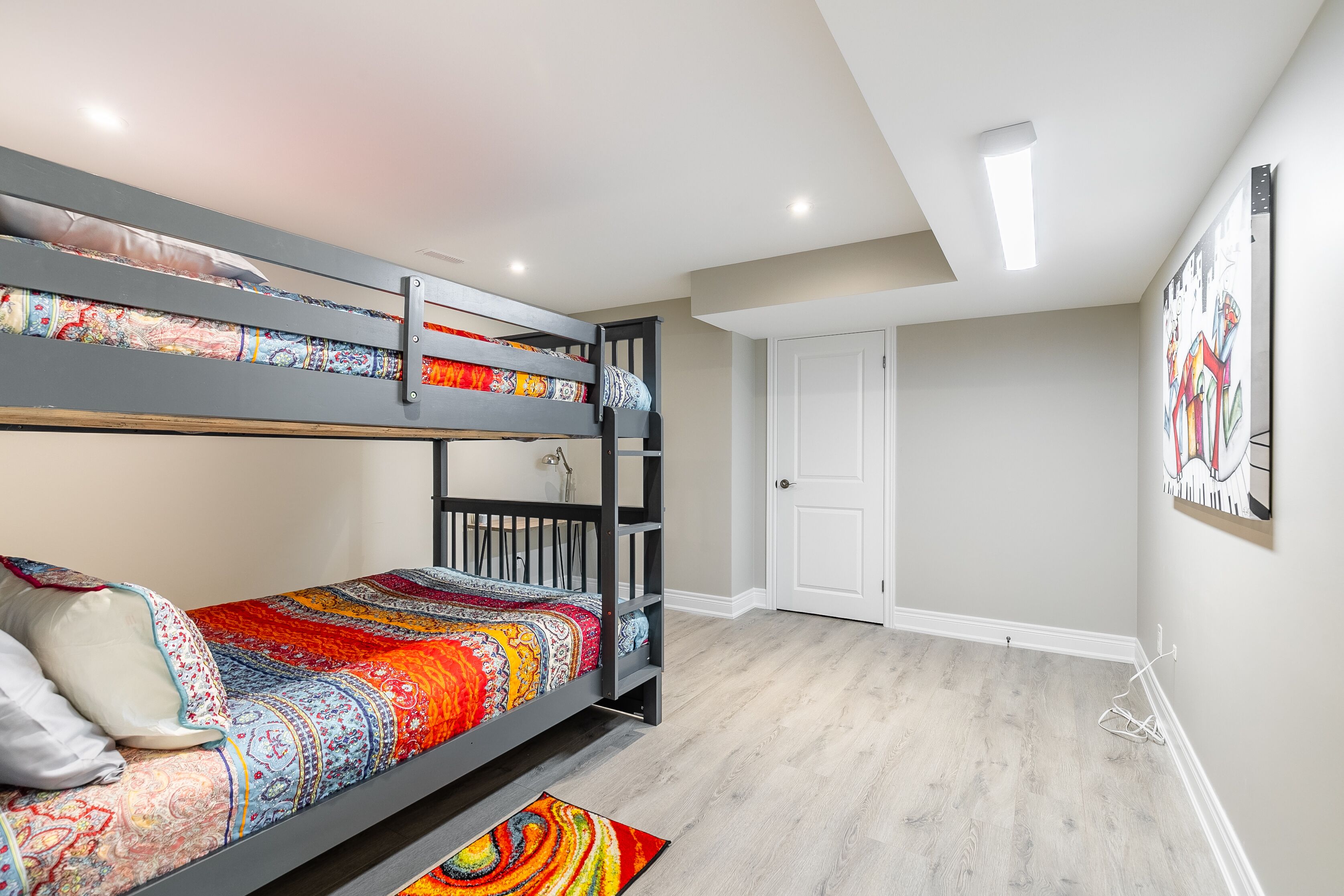 Een stapelbed met kleurrijke beddengoed, een witte deur en een schilderij aan de muur.