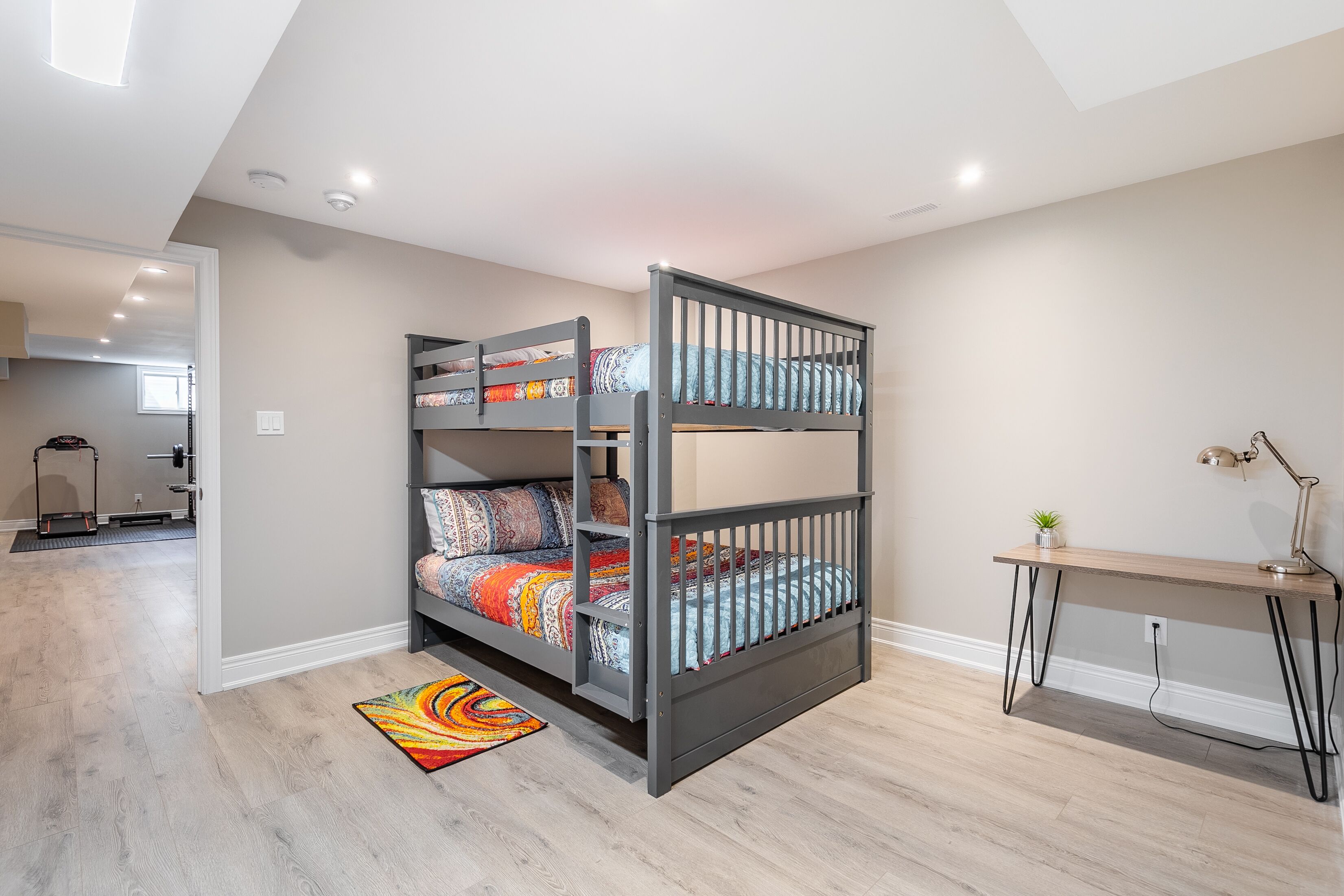 A bunk bed with colorful bedding, a desk with a lamp, and a small plant.