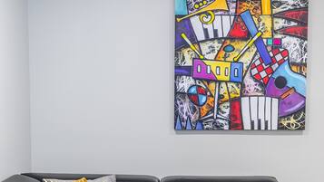 Un canapé d’angle en cuir noir agrémenté de deux coussins à motifs, un tableau abstrait aux couleurs vives accroché au mur et un plaid multicolore posé sur le sol.