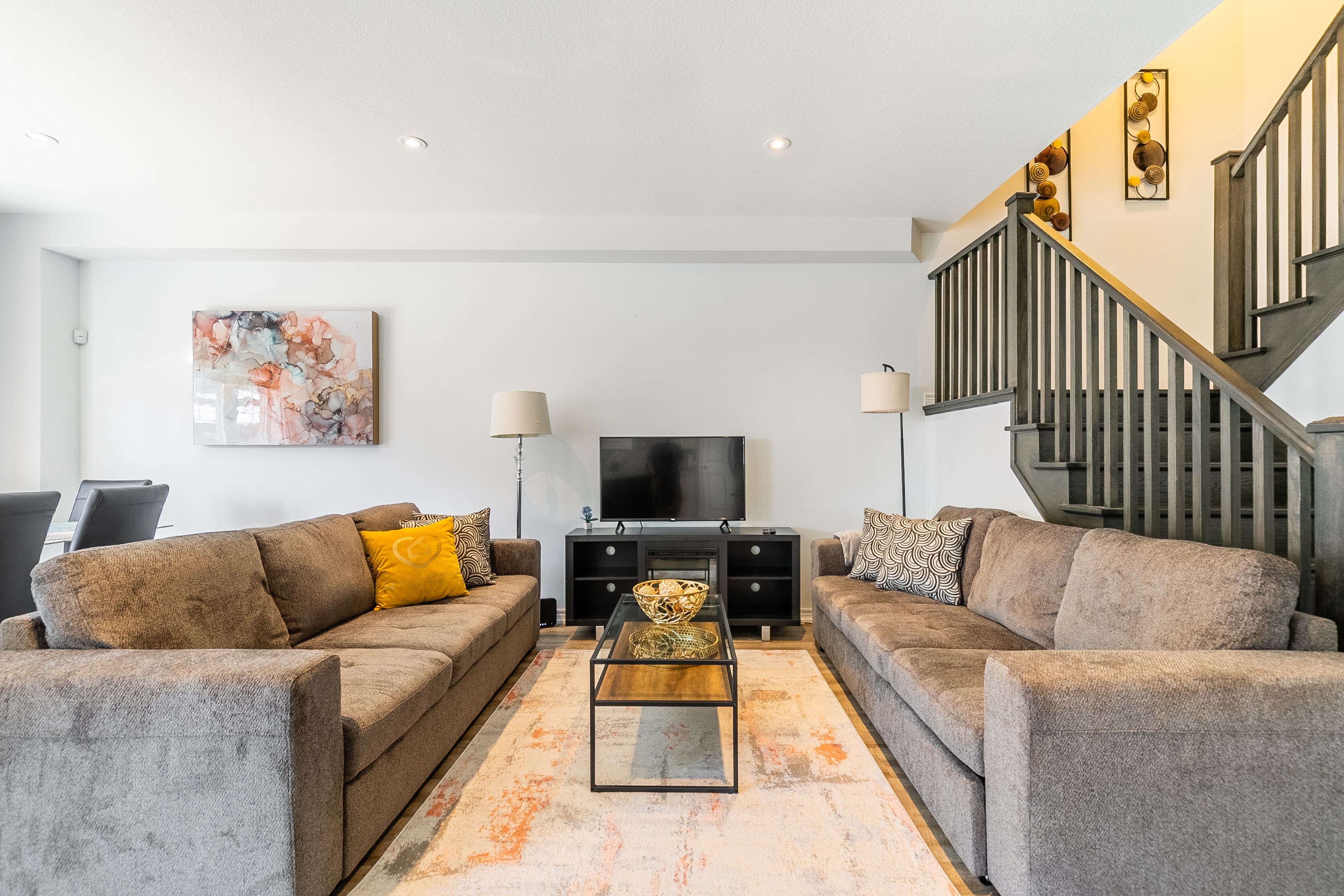 A modern living room with two sofas, a coffee table, a TV, and a staircase.