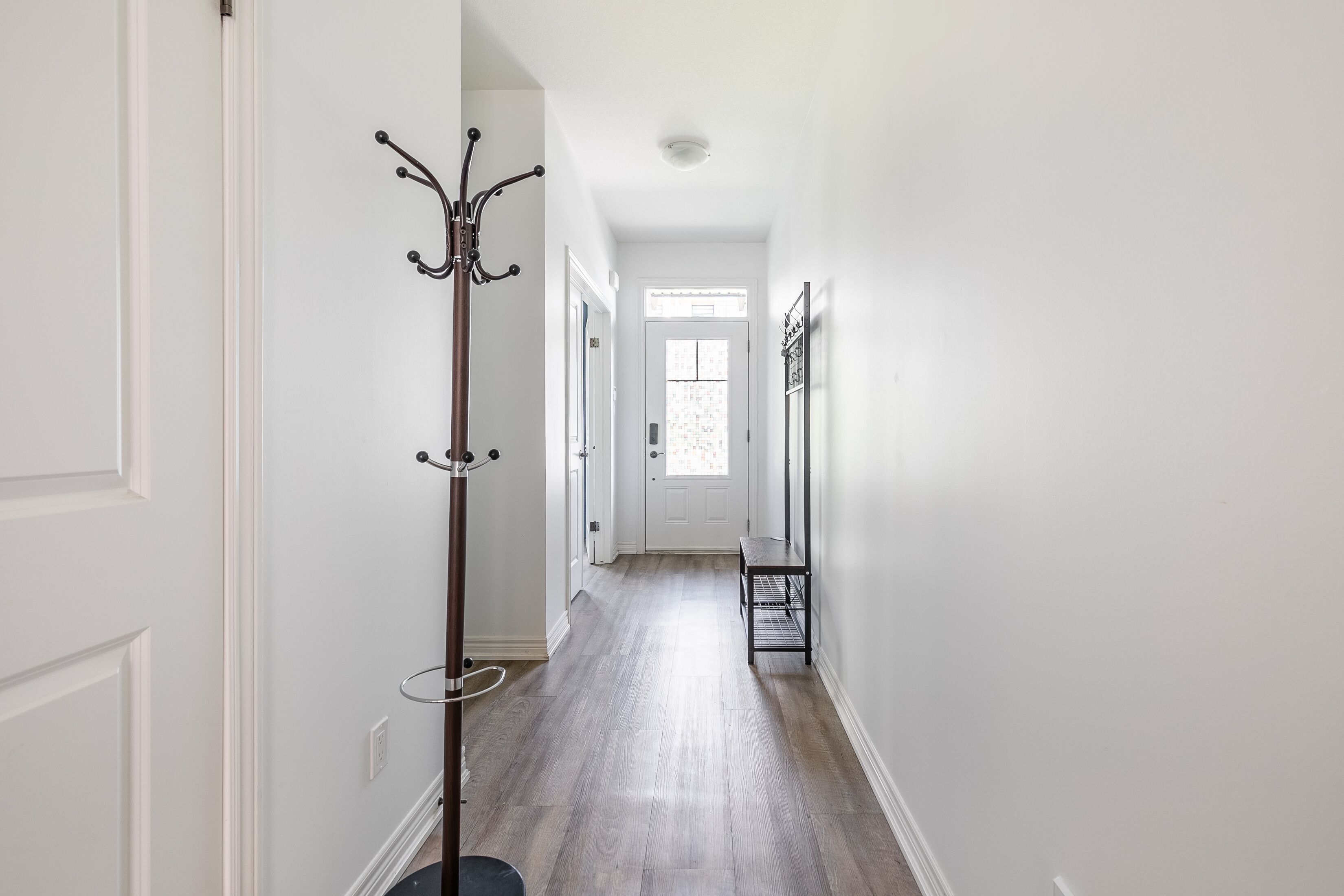 A hallway with a coat rack, a bench, and a door at the end.