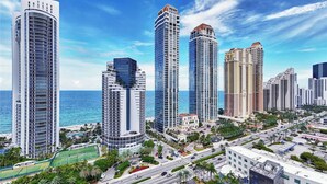 A high-rise urban area with multiple skyscrapers, a clear blue sky, and a view of the ocean.
