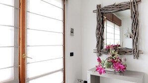 Una habitación con puerta de madera, un espejo con marco rústico y un florero con flores rosadas sobre una consola blanca.