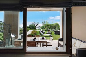 Blick durch eine Glastür auf einen Außenbereich mit Terrasse, Tisch, Stühlen und einer Couch.