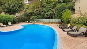 Piscina con sillas de descanso, rodeada de árboles y un edificio.