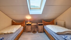 Un dormitorio cálido y acogedor en el ático, con tragaluces, dos camas de madera, una mesita y una lámpara.