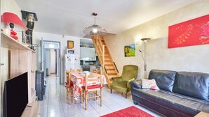 Una sala de estar con un sofá, un tapete rojo, una escalera de madera y un comedor con mesa y sillas.